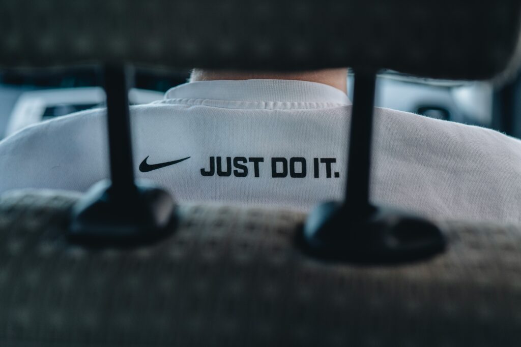 The Nike swoosh and the words "Just do it", a brand asset used famously by Nike, appear on the back of a person's shirt through the gap in a car headrest's support pillars.